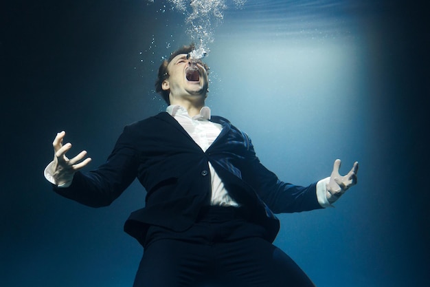 A businessman a man in a suit screams underwater