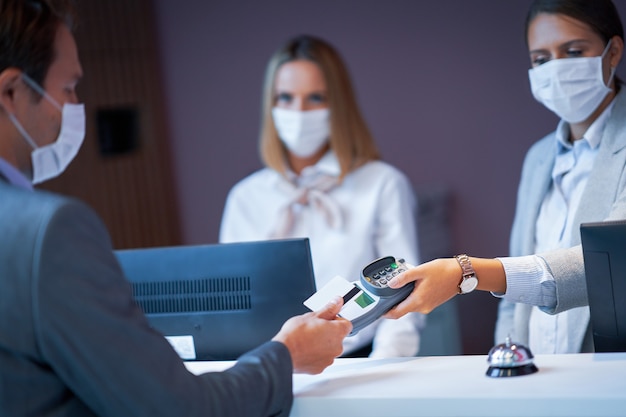 Uomo d'affari in maschera alla reception di un hotel che fa il check-in