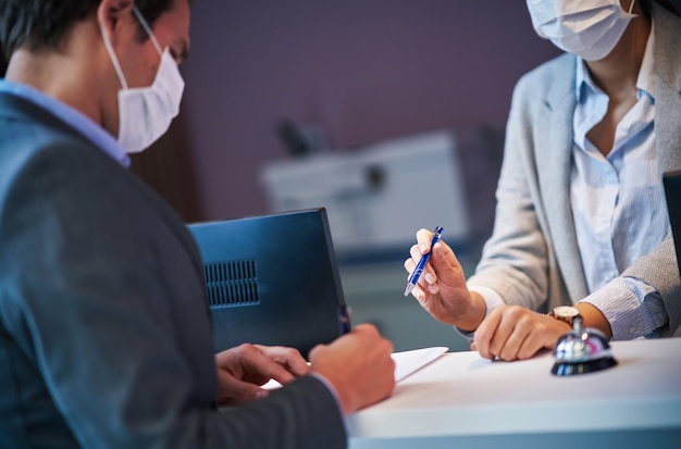 businessman in mask at the reception of a hotel checking in