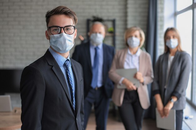 Photo businessman in medical mask with colleagues in the background in office.