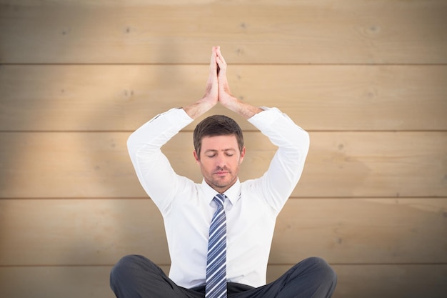 Businessman meditating in lotus pose against bleached wooden planks background