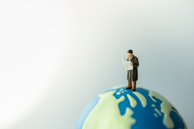 Photo businessman miniature figure people standing and reading a newspaper on mini world ball.