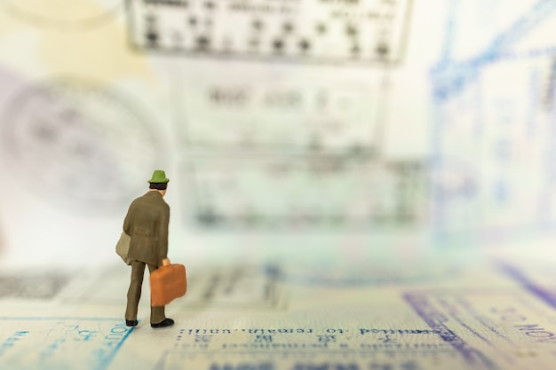 Businessman miniature figure people with baggage standing on passport with immigration stamped