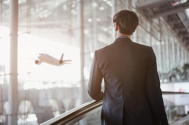 空港で荷物を持ってチェックインするためにエスカレーターでターミナルゲートに移動するビジネスマン。