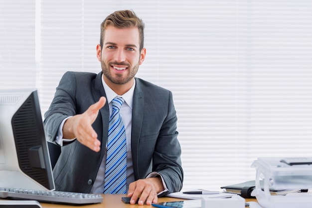 Businessman offering a handshake at office desk