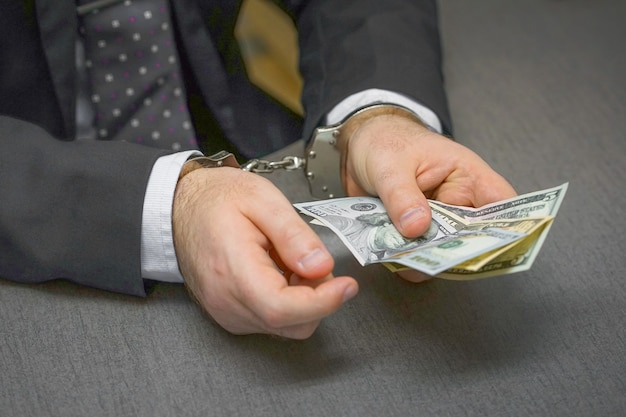 Businessman in office in handcuffs holding a bribe. Selective focus