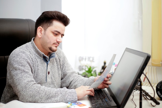 Businessman at office, he is working with a computer, checking paper and bills.