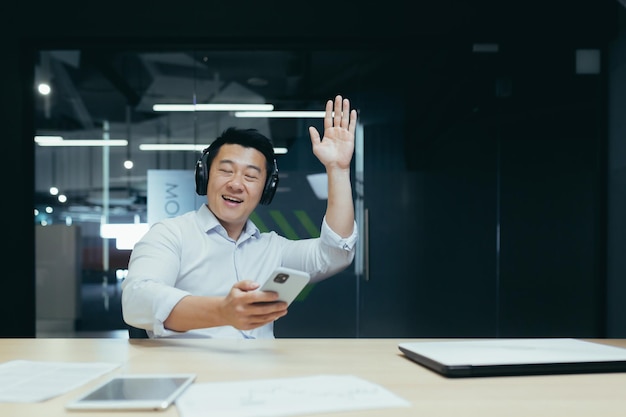 Uomo d'affari in ufficio che riposa durante la pausa di lavoro ascoltando musica in grandi cuffie nere uomo asiatico