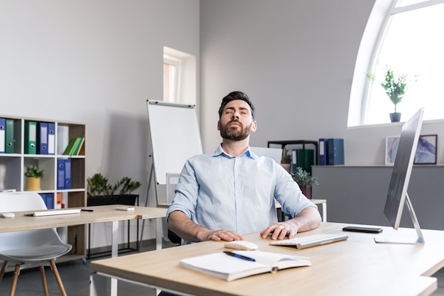 L'uomo d'affari in ufficio con gli occhi chiusi esegue esercizi di respirazione libero professionista che lavora al computer