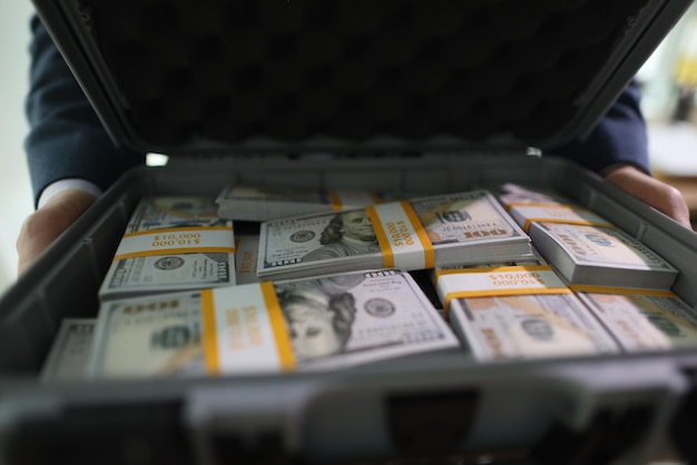 businessman opens big suitcase with stacks of dollar bills in office successful man