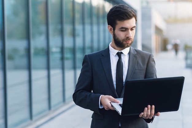 Businessman outdoors on a background of cityscapes holding a laptop looking into it. 