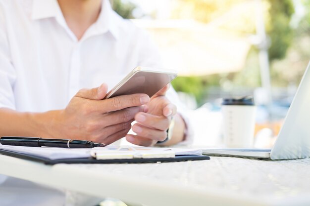 Uomo d'affari on park bench che manda un sms sullo smartphone all'aperto nel giardino