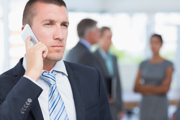 Businessman on the phone with colleagues behind him