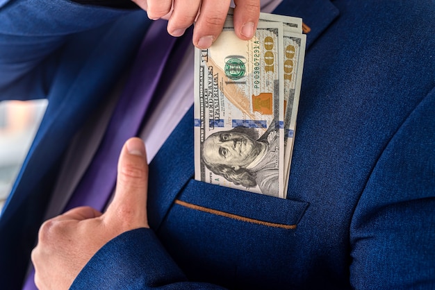 Businessman placing dollar money into his pocket as after a\
successful deal or bribe. corrupt concept