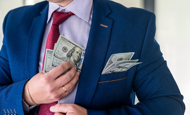 Businessman placing dollar money into his pocket as after a\
successful deal or bribe corrupt concept