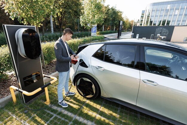 Photo businessman plugging in charging cable to to electric vehicle male hand inserts power connector into