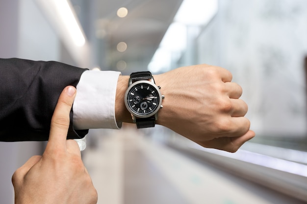 Businessman pointing at hand watch on grey