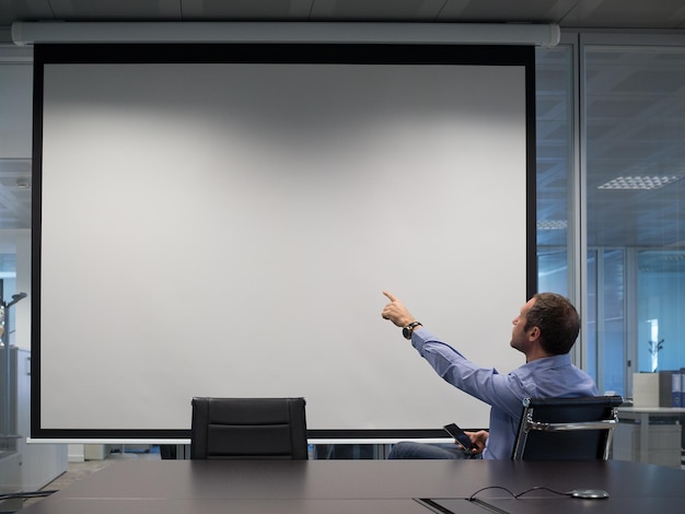 Foto uomo d'affari che indica lo schermo di proiezione durante una riunione in ufficio