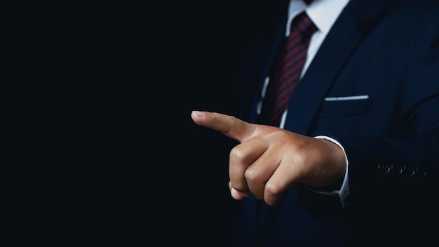 Businessman pointing to something or touching a touch screen on black background copy space