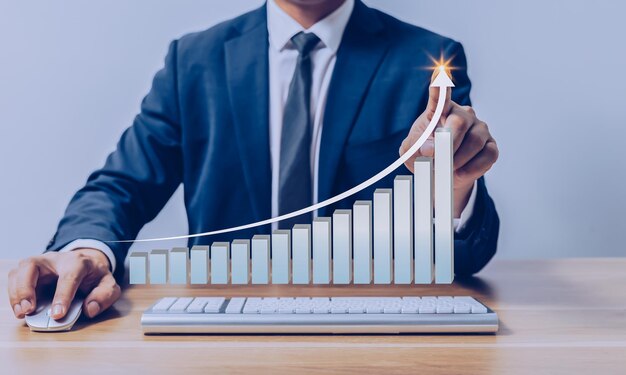 Businessman pointing to virtual investment bar and line graph on wooden table as business strategy and stock value investor concept