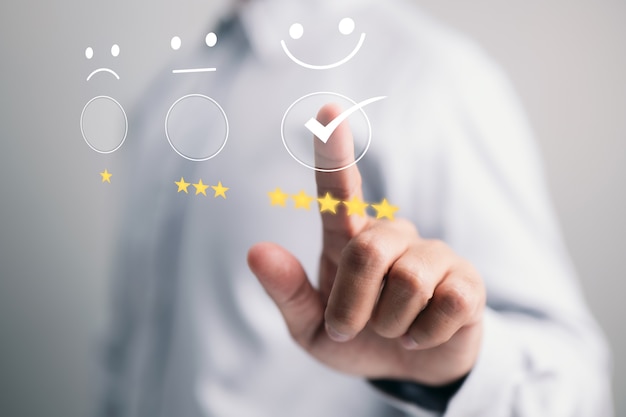 businessman presses a smiling face emoticon on a virtual touch screen. concept of customer service evaluation.