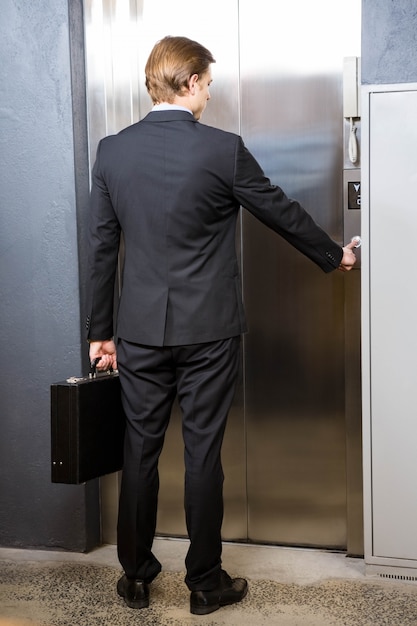 Businessman pressing elevator button in office