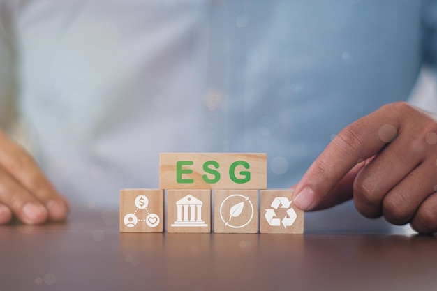 Бизнесмен нажимает пальцем на деревянные кубики с ESG на деревянном бруске. Это идея для устойчивого организационного развития. â€‹учет окружающей среды, общества и корпоративного управления