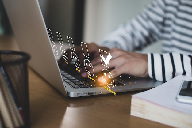 Foto uomo d'affari premendo l'emoticon del viso sul laptop sulla scrivania e selezionando l'icona della faccina sorridente e una valutazione a 5 stelle dimostra che la soddisfazione del cliente è essenziale per un business di successo