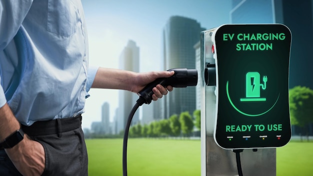 Бизнесмен вытаскивает зарядное устройство для электромобиля, чтобы подзарядить аккумулятор своего электромобиля от зарядной станции на фоне зеленого эко-городского парка. Будущий инновационный электромобиль и энергетическая устойчивость.