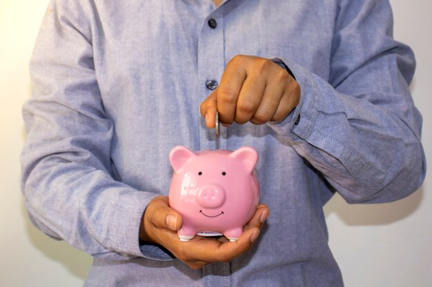 A businessman put a coin in a pink piggy bank and saved the money to plan ideas for future retirement funds.