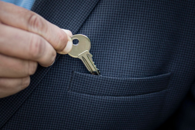 Businessman puts a small key to a safe deposit box or a bank in
his jacket pocket the concept of saving money the real estate agent
takes out the key to the apartment