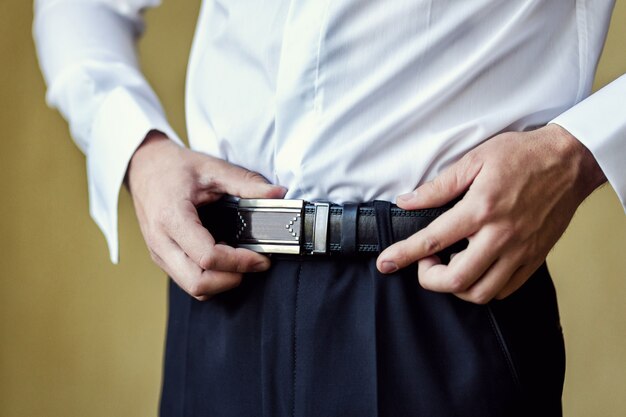 Uomo d'affari che indossa una cintura. l'uomo mette la cintura marrone. focus sulla fibbia. sposo tenendosi per mano sulla cintura, abito da sposa