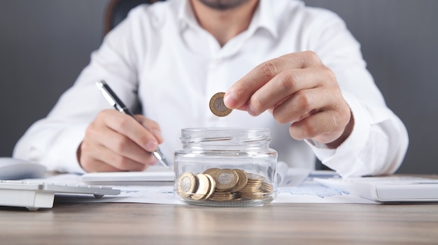 Businessman putting coin in glass bank. Saving money