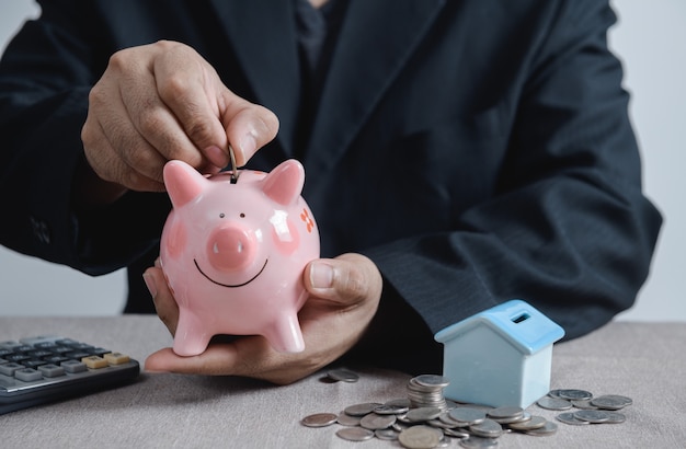 Businessman putting coin into the piggy bank, saving for new house concept