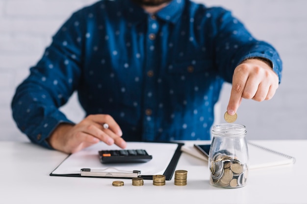 Photo businessman putting coins in jar using calculator at workplace