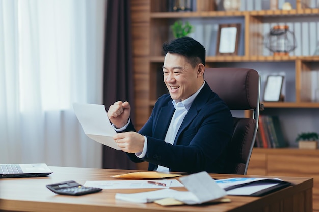 Businessman received good news by mail Asian works in a classic office at the table happily reads the letter