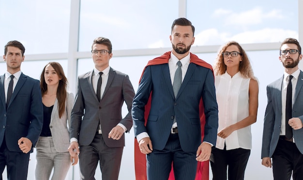赤いスーパーヒーローのマントを着たビジネスマンとコピースペースを持つ彼のビジネスチームの写真