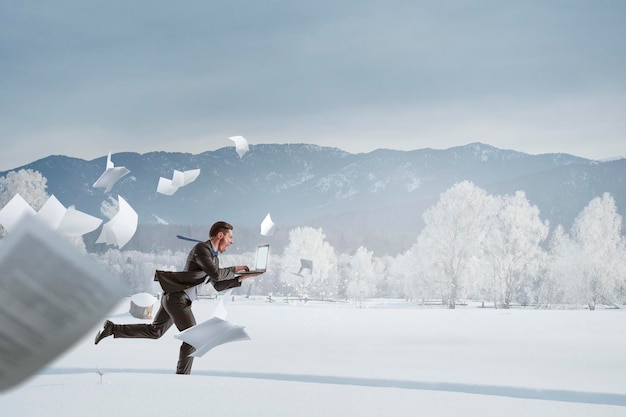 Businessman running among snow countryside at winter. Mixed media