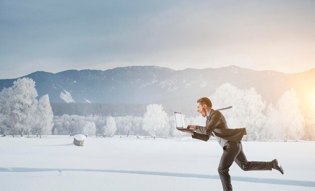 Businessman running among snow countryside at winter. Mixed media