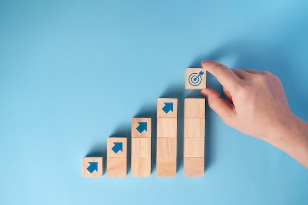 Businessman's hand arranging wooden blocks staircase with arrow icon, Business planning concept.