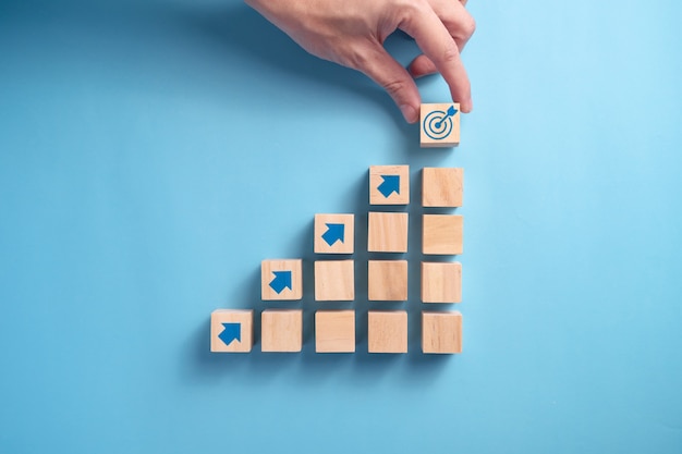 Businessman's hand arranging wooden blocks staircase with arrow icon, Business planning concept.