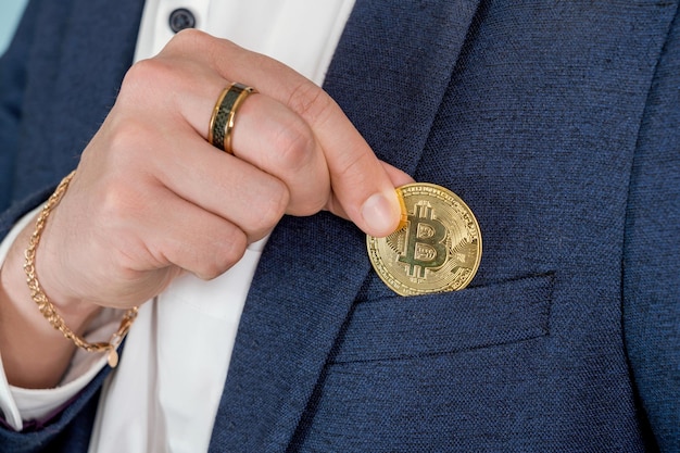 The businessman's hand drops a gold bitcoin coin into the breast pocket of his jacket