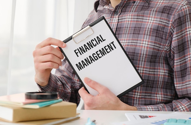 Businessman's hand holding paper business card with text financial management, closeup light blue background, business concept