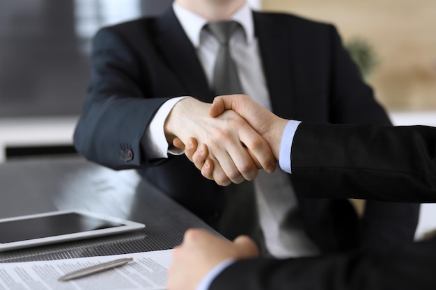 Businessman shaking hands with his colleague or partner above the glass desk in modern office closeup Unknown business people at meeting Teamwork partnership and handshake concept