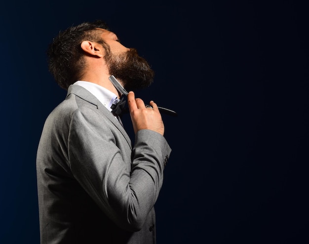 Businessman shaves on dark blue background Macho in formal suit