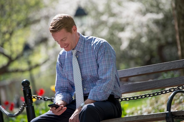 A businessman in a shirt with white tie sitting on a park bench under the shade of a tree with bloss