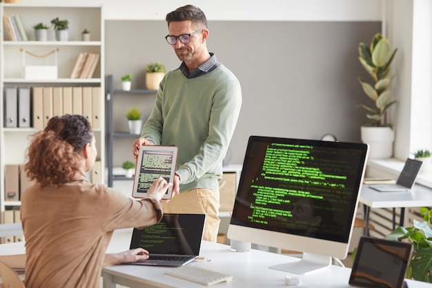 Uomo d'affari che mostra il software su tablet pc al suo collega mentre lavorano al servizio informatico