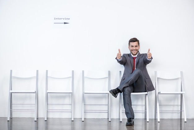 Foto uomo d'affari che mostra i pollici in su e aspetta il colloquio in ufficio, concetto di affari