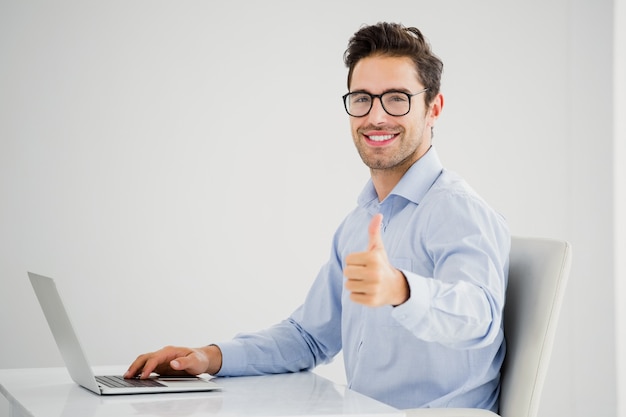 Businessman showing thumbs up while using laptop