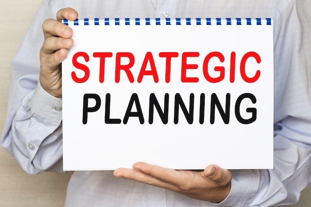 The businessman shows a sheet with the text strategic planning on a white background